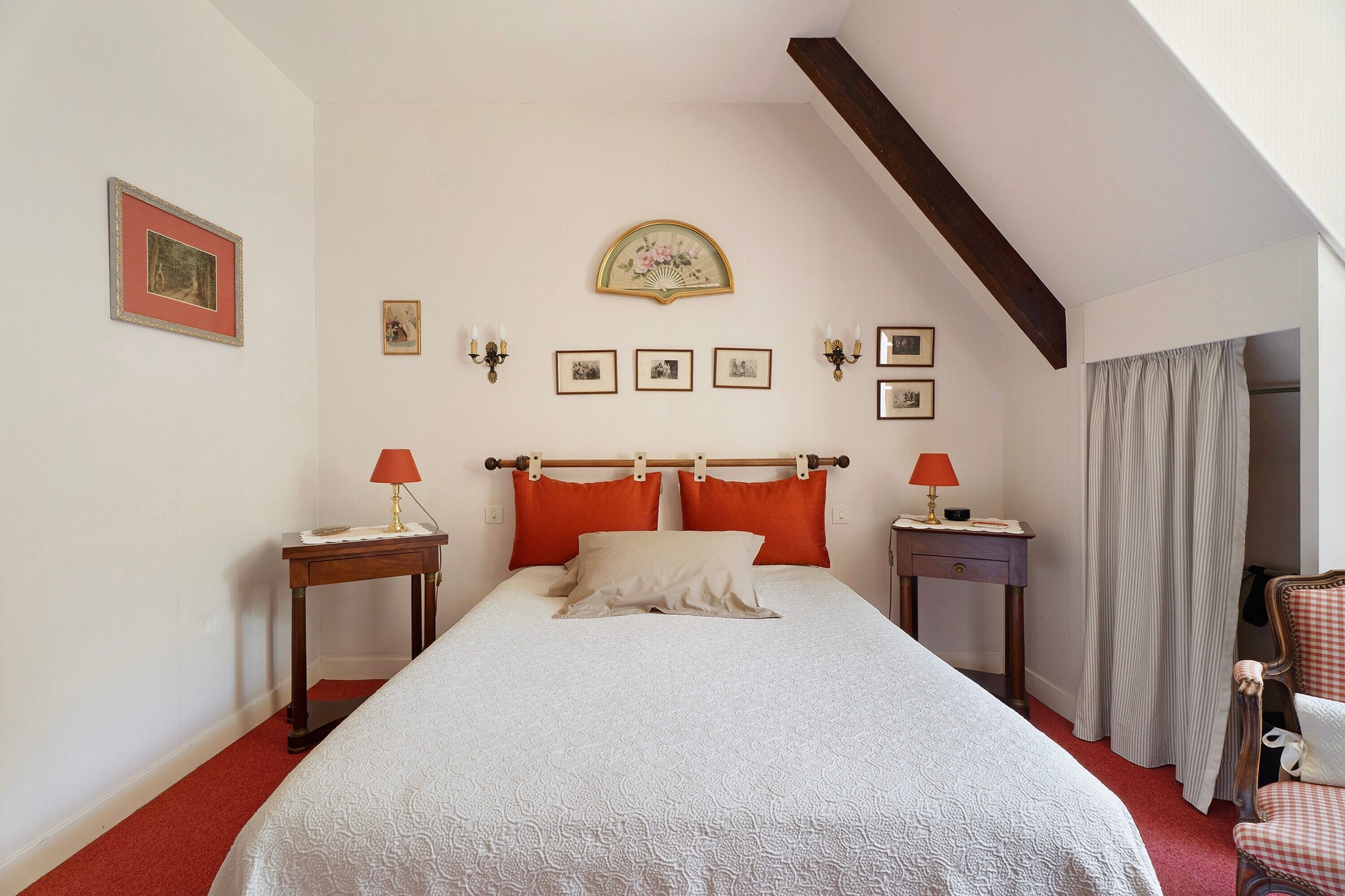 Une chambre à coucher comprenant un lit, deux tables de chevet, une commode, une chaise, une fenêtre avec des rideaux et un plafond en pente.