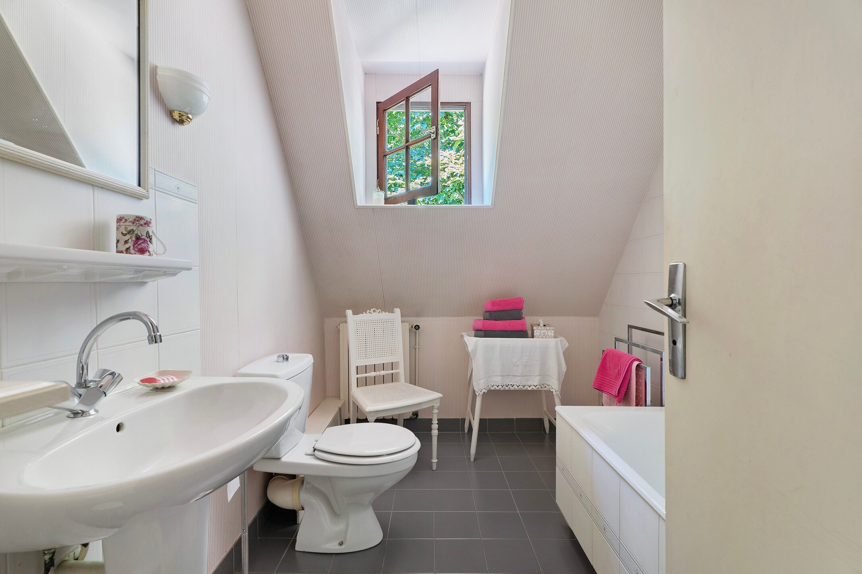 Un bagno piccolo e moderno con lavandino, water e vasca da bagno bianchi. C’è una finestra con vista sul verde circostante.