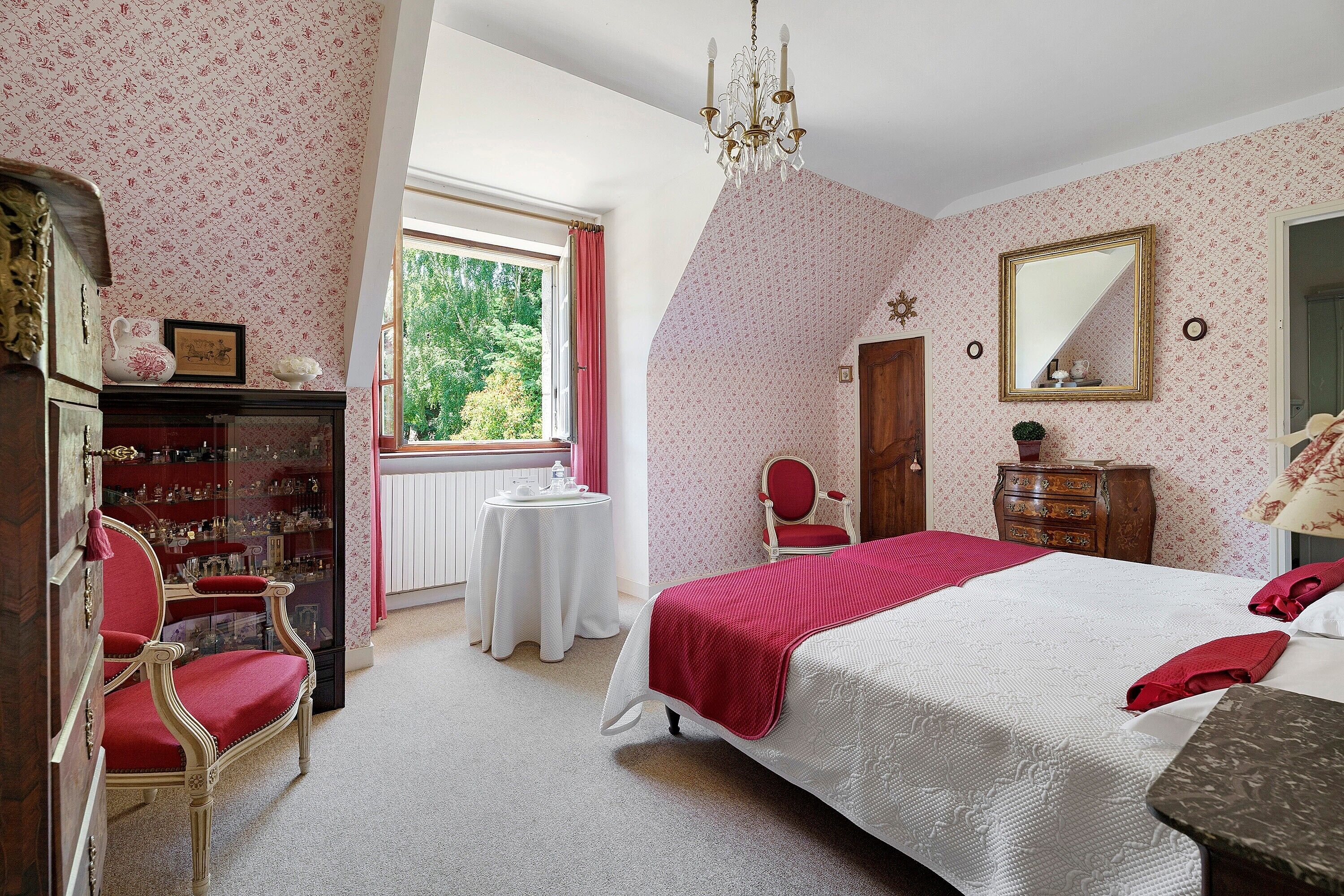 A bedroom with a large bed, a chandelier, a dresser, a chair, and a window with curtains.