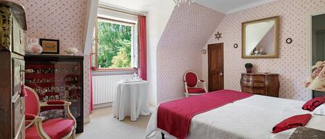 Um quarto com uma cama grande, um candelabro, uma cômoda, uma cadeira e uma janela com cortinas.