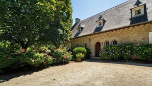 A stone building with a gravel driveway and lush greenery.