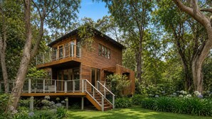 Eine zweistöckige Holzhütte mit Balkon, umgeben von üppigem Grün und Bäumen.