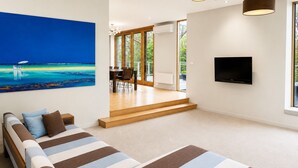 Ein modernes Wohnzimmer mit einem großen Gemälde, einer Couch, einem Fernseher und einer Treppe, die zu einem Außenbereich führt.