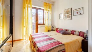 Une chambre à coucher avec un lit, des rideaux, une fenêtre, un radiateur, une lampe et deux tableaux encadrés accrochés au mur.