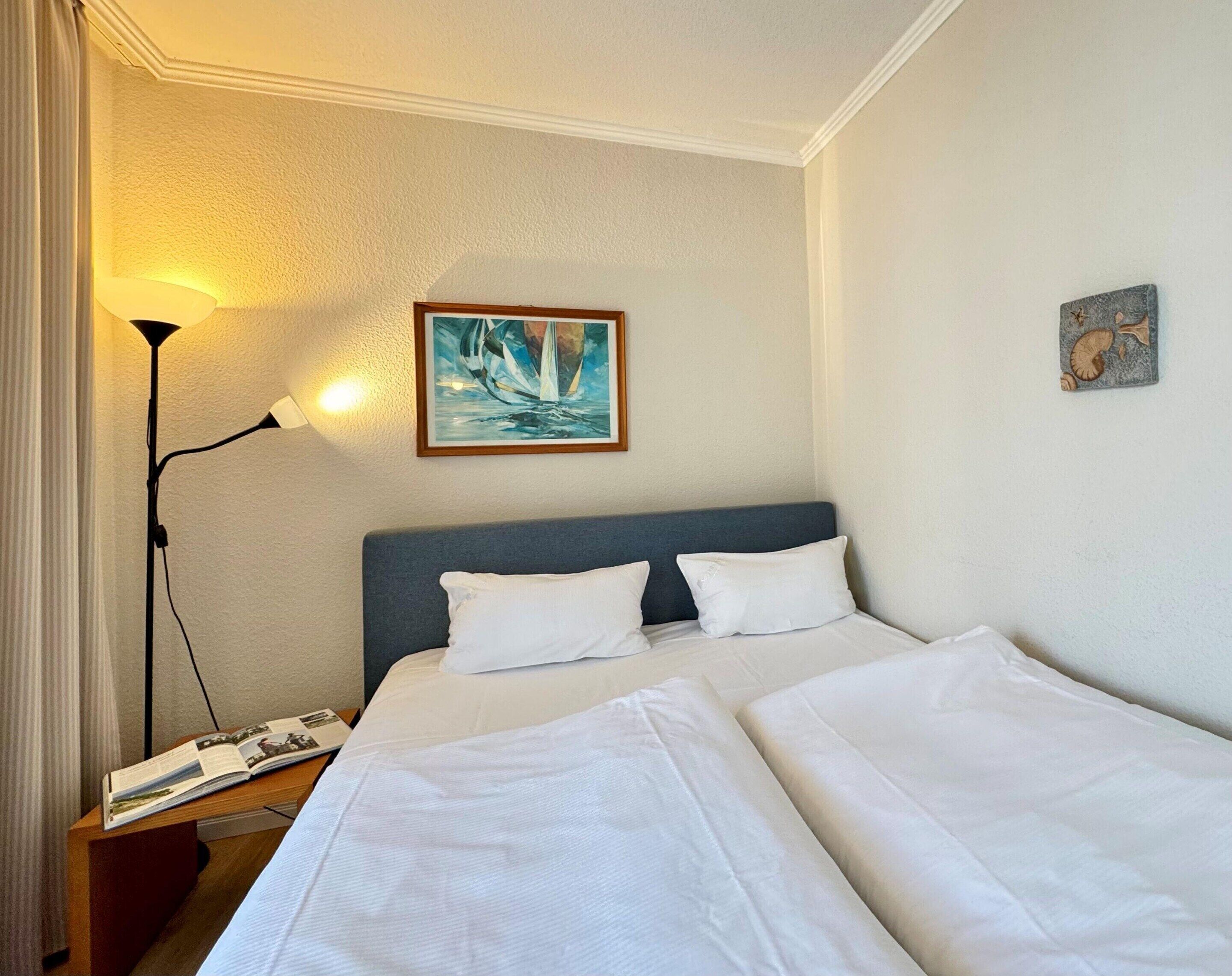 A hotel room with a bed, a nightstand, a lamp, and a painting on the wall.