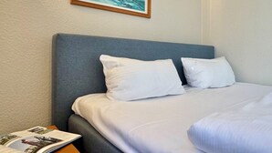 A neatly made bed with white linens, a grey headboard, and a framed painting of sailboats above it. - Studio mit Balkon im Seepark Sellin (Sellin)