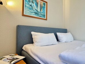 A neatly made bed with white linens, a grey headboard, and a framed painting of sailboats above it. - Studio mit Balkon im Seepark Sellin (Sellin)