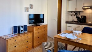 A compact living space with a TV, wooden furniture, a dining table set for two, and a kitchen area. - Studio mit Balkon im Seepark Sellin (Sellin)
