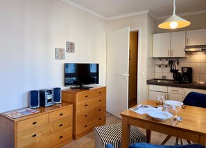 A compact living space with a TV, wooden furniture, a dining table set for two, and a kitchen area. - Studio mit Balkon im Seepark Sellin (Sellin)