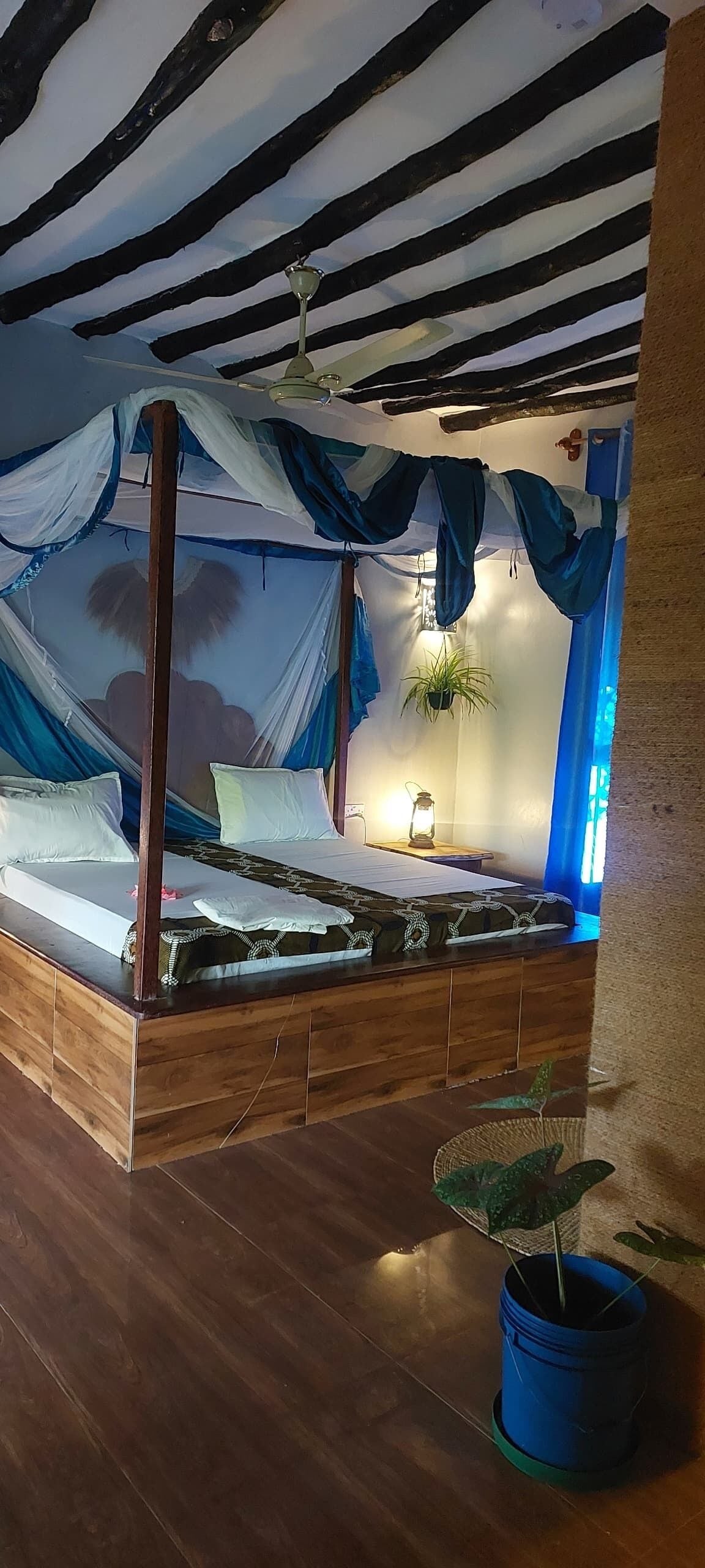 Un lit à baldaquin, une plante en pot et une table de chevet avec une lanterne.