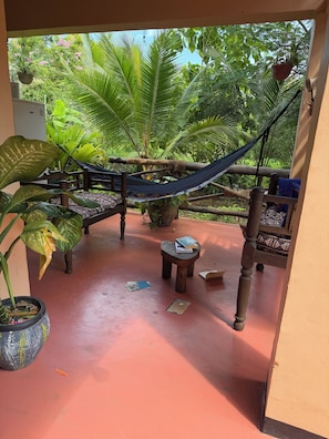 A hammock, wooden furniture, and potted plants in a covered outdoor area.