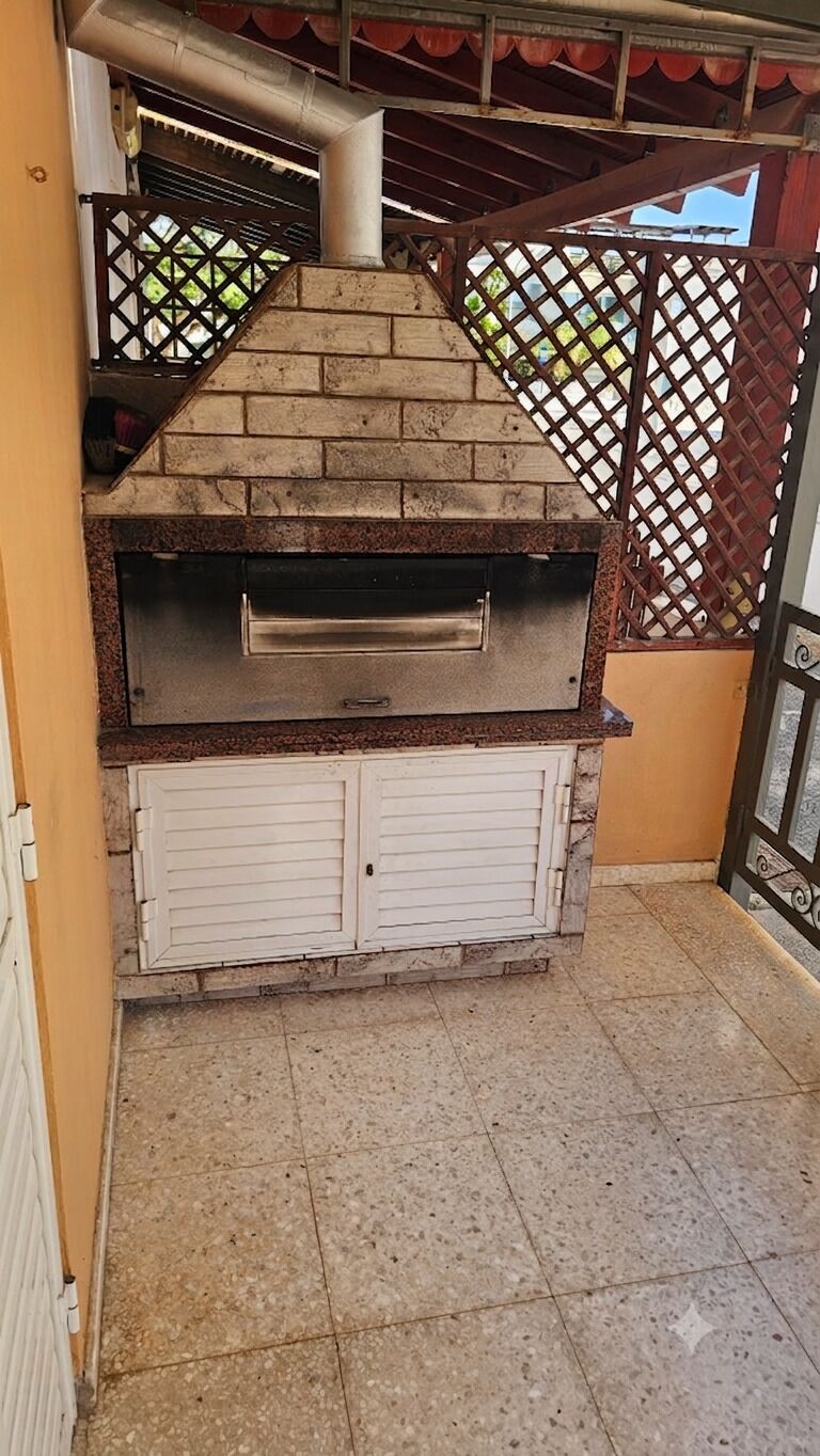 A brick-built outdoor oven with a metal door, set against a wall with a lattice design.
