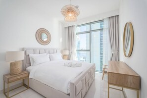 A modern hotel room with a large bed, bedside lamps, a wooden desk, and a large window with curtains. - FIRST CLASS |1BR| Sea Views | Direct Beach Access (Dubai Harbour)