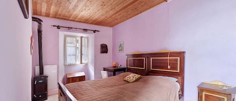 Un dormitorio con techo de madera, una cama con colcha acolchada, una mesita de noche, un aparador y un radiador.