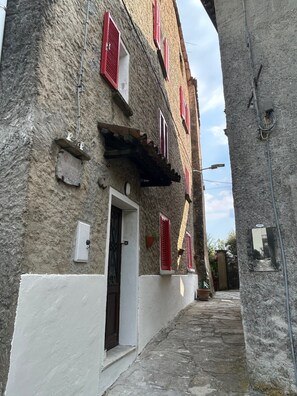 A narrow street with a building featuring red shutters and a white door.