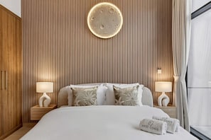 A hotel room with a bed, two bedside tables, a wall-mounted light, and a window with curtains. - FIRST CLASS | 2BR | Luxury Escape in Meydan (Meydan)