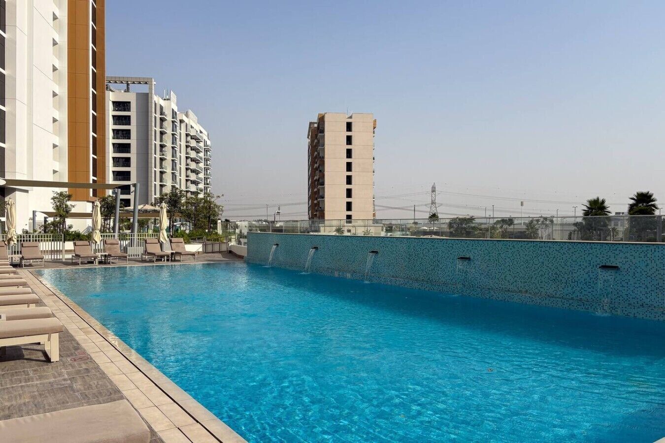 A swimming pool with lounge chairs and a tiled wall.