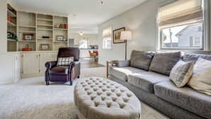 Una sala de estar con sofá, reposapiés y sillón, un ventilador de techo y una estantería.