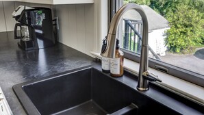 Una cocina con un lavamanos de acero inoxidable, una cafetera y dos botellas de jabón en la encimera.