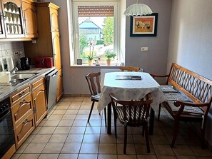 A kitchen with wooden cabinets, a dining table with chairs, a window with a view of greenery, and a pendant light. - Holiday Home in Badem (Badem)