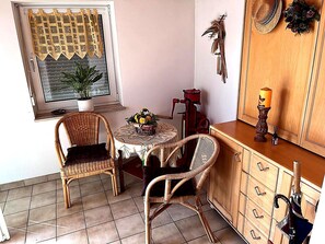 A small dining area with wicker chairs, a table with a woven tablecloth, a potted plant, and a window with decorative curtains. - Holiday Home in Badem (Badem)