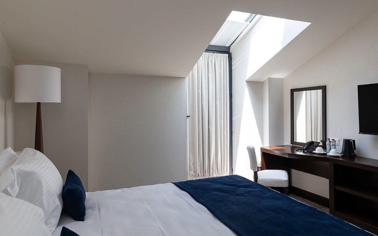 Hotelkamer met een bed, bureau, stoel, lamp, spiegel en dakraam.