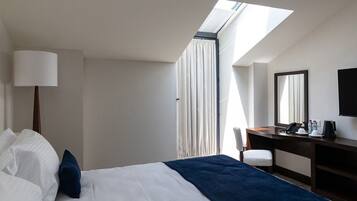 Hotelkamer met een bed, bureau, stoel, lamp, spiegel en dakraam.