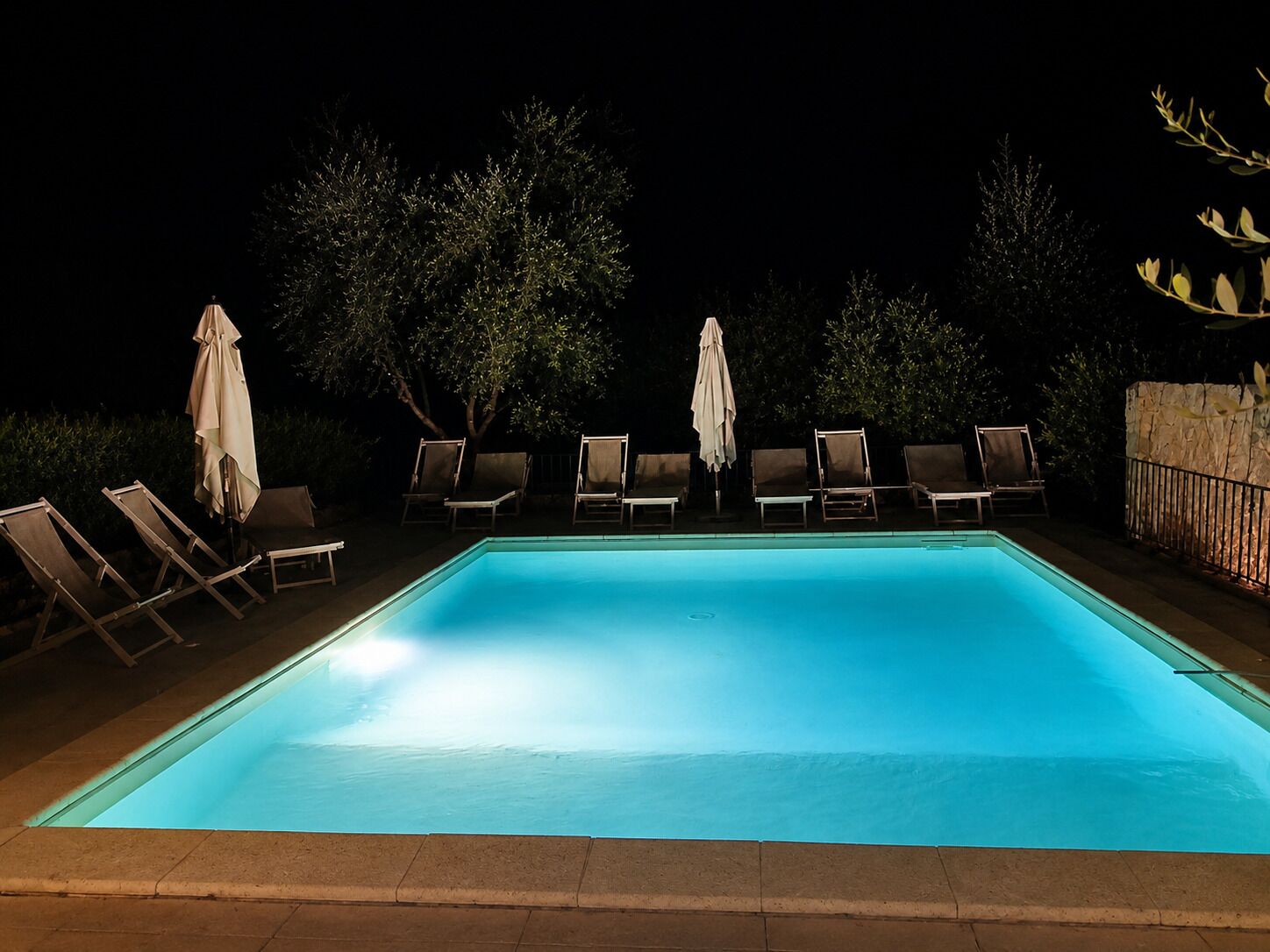 Une piscine rectangulaire à l’eau d’un bleu clair, entourée de chaises longues et de parasols.