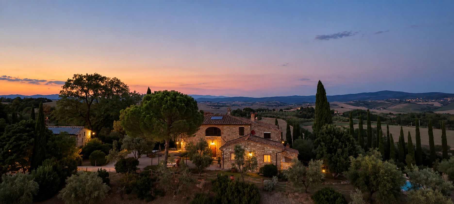 A stone villa with a garden, surrounded by trees and hills.
