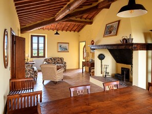 A dining area with a wooden table and chairs, a sofa, and a fireplace with cooking utensils. - "La Quercia" Tuscan Farmhouse with Fireplace, 3 Bedrooms, and a Pool (Toscana)