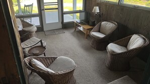 A room with wicker furniture, a table, and a view of greenery outside. - Location, Location, Location! (Westerly)