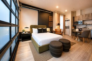 Una habitación de hotel moderna con una cama grande, un escritorio, una silla y una kitchenette.