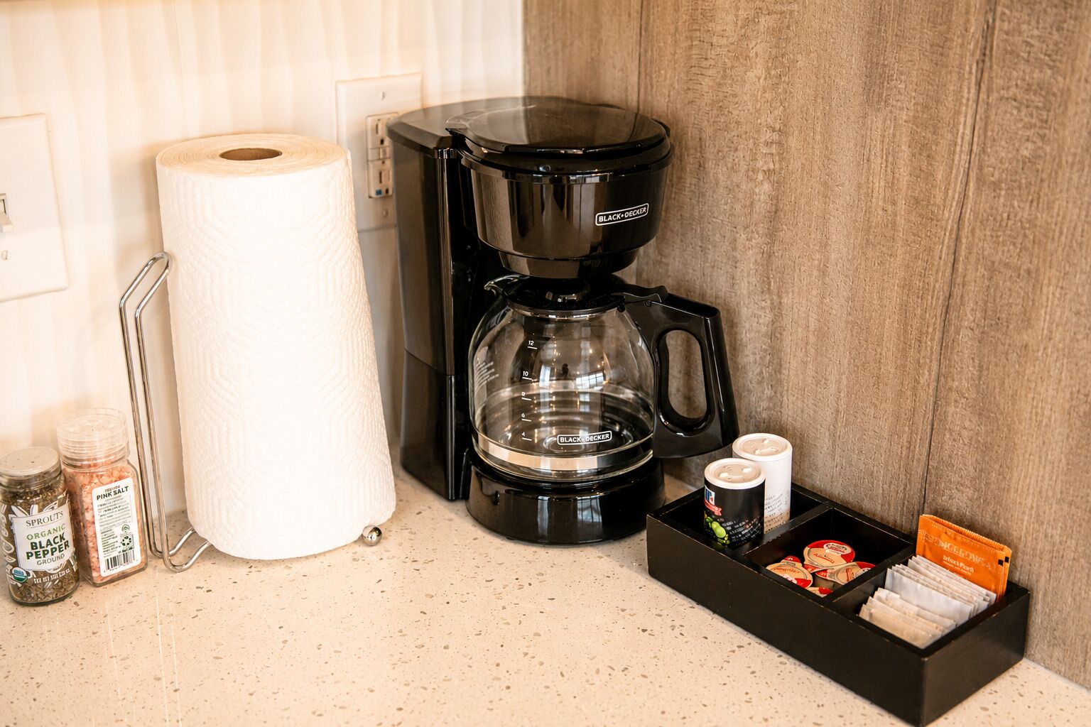 A coffee maker, a roll of toilet paper, and a spice rack with jars on a countertop.