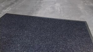 Une terrasse couverte, aménagée avec des meubles en osier, une table basse en verre et un tapis foncé.