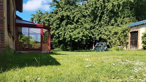 Un espace verdoyant avec un patio fermé par des baies vitrées, un grand arbre et un bâtiment doté d’un toit rouge.