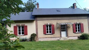 Une maison à deux étages avec une façade en briques, des volets rouges et un petit porche à l’avant.