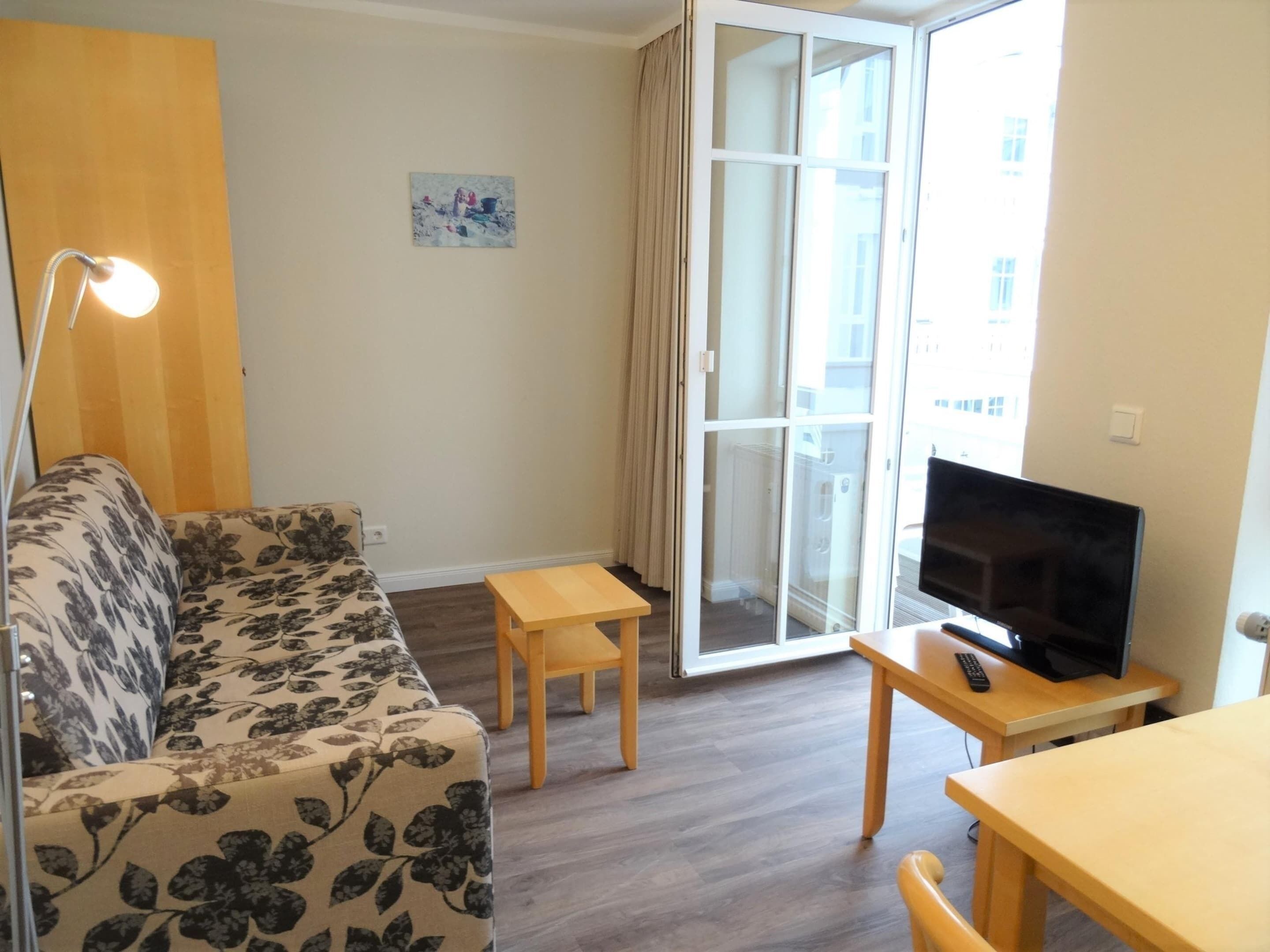 Un salon comprenant un canapé, une petite table, un téléviseur et une porte-fenêtre coulissante donnant sur un balcon.