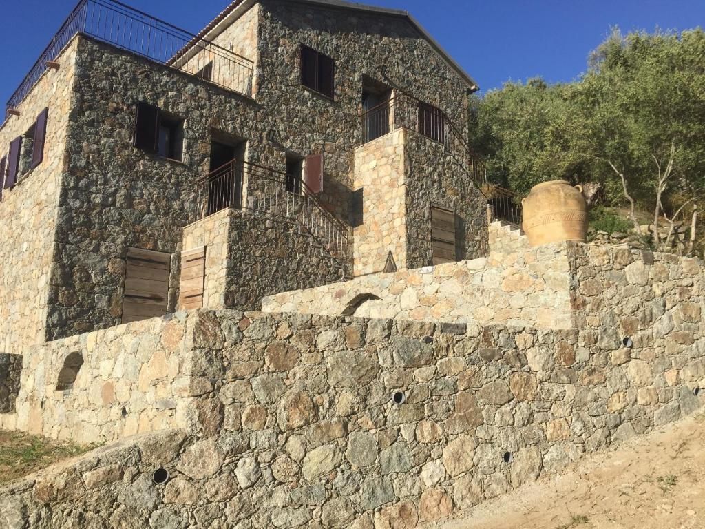 Un bâtiment en pierre doté de nombreuses fenêtres et d’un balcon, situé sur une colline, sous un ciel dégagé.