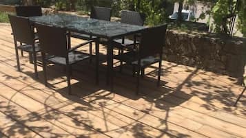An outdoor patio with a table and chairs, surrounded by greenery and a stone wall.