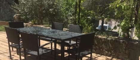 An outdoor patio with a table and chairs, surrounded by greenery and a stone wall.