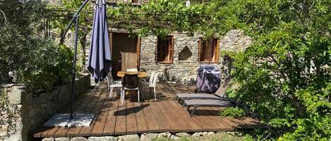 A rustic outdoor seating area with a table and chairs, a covered table, and a hanging umbrella.
