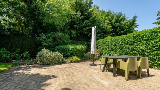 An outdoor patio area with a table and chairs, surrounded by lush greenery and a hedge. - 4-guest Bungalow Near Texel Dunes (De Koog)