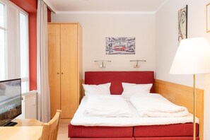 A hotel room with a bed, a TV, a wooden wardrobe, and a painting on the wall. - Gemutliche Ferienwohnung fur Zwei in Sellin mit Balkon (Sellin)