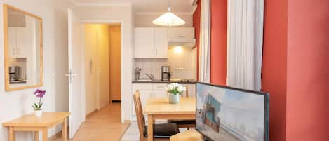 Una cocina moderna con armarios blancos, un comedor con mesa y sillas de madera, y un televisor sobre un mueble.