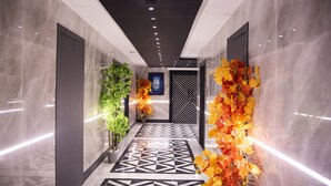 A hallway with a geometric patterned floor, a black and white decorative door, and artificial plants with autumn leaves.
