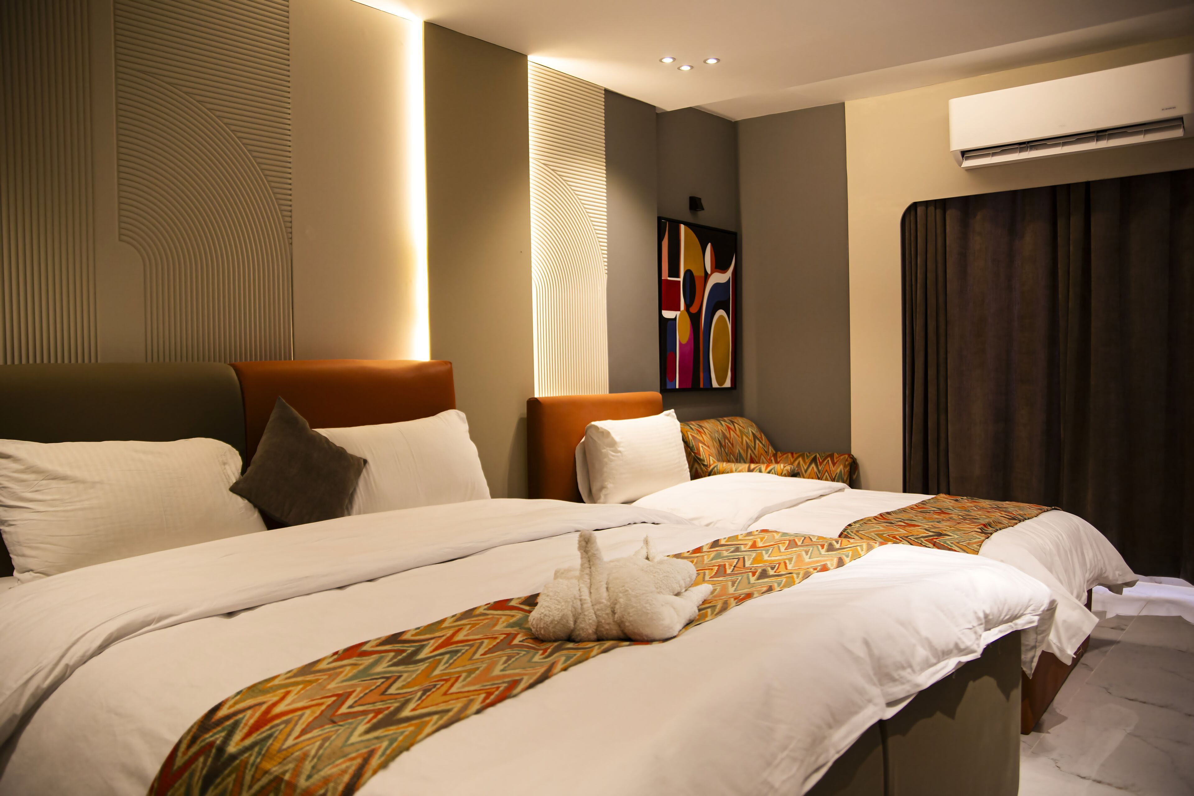 Habitación de hotel con dos camas, una gran obra de arte en la pared y un equipo de aire acondicionado.