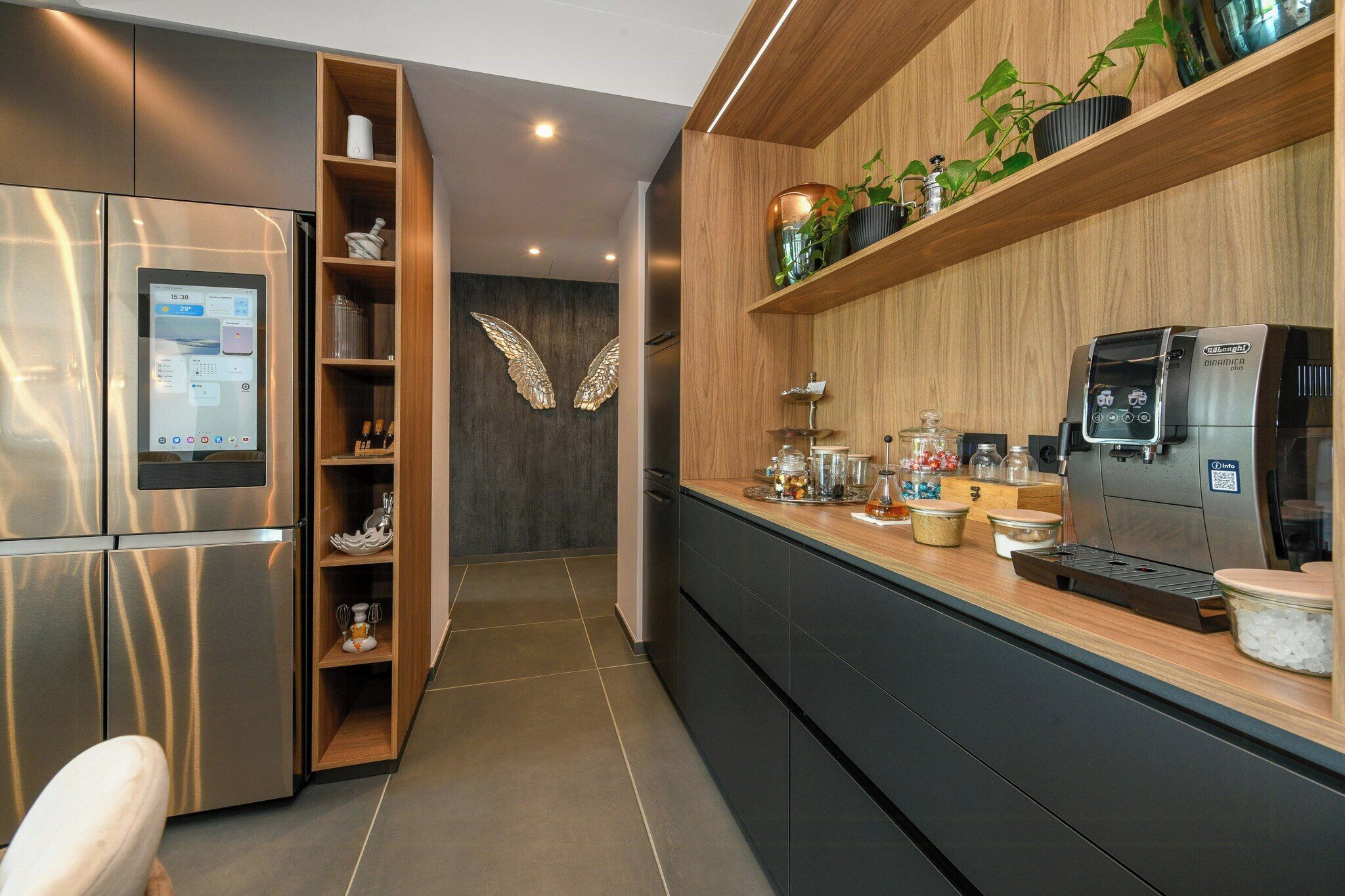 Een moderne keuken met een ingebouwde koffieapparaat, een koelkast en houten planken met planten.