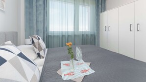 Un dormitorio con una cama, una mesita de noche con un jarrón y un vaso, una ventana con cortinas y un armario.