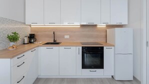 Una cocina moderna con armarios blancos, un horno negro y un refrigerador blanco.