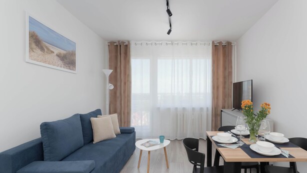 Una sala moderna con un sofá azul, una mesa de comedor con platos y vasos, y un televisor en la pared.